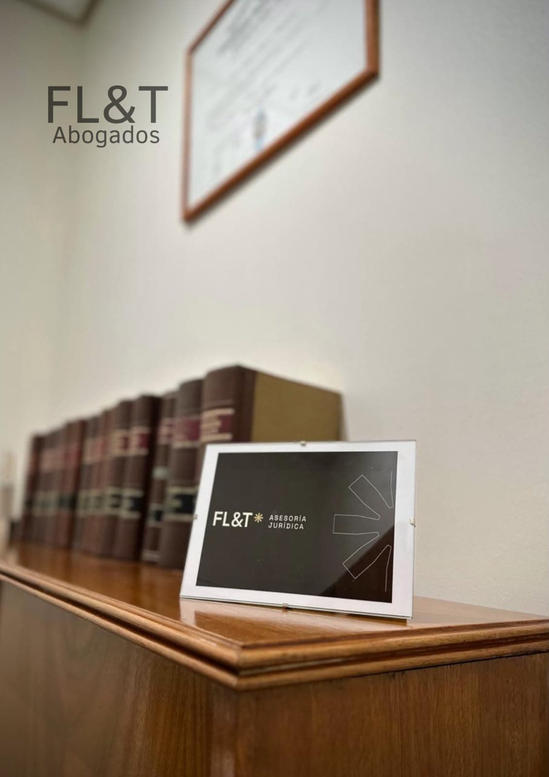 Cartel de FL&T Asesoría Jurídica junto a libros de derecho y diploma en la oficina